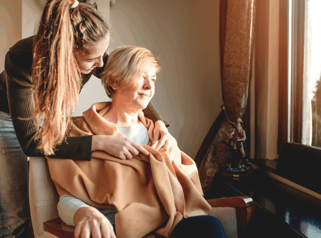 A woman gently helps an older woman wrap a blanket around her shoulders for warmth and comfort.